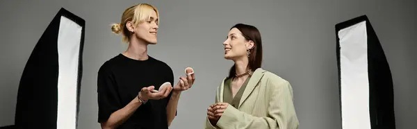 stock image A man applies makeup on a woman in front of a gray wall.