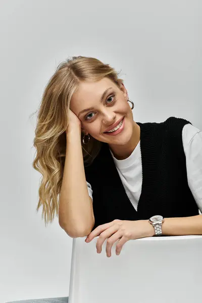 stock image A young, beautiful woman with blonde hair sitting at a table, looking contemplative with her hand on her head.