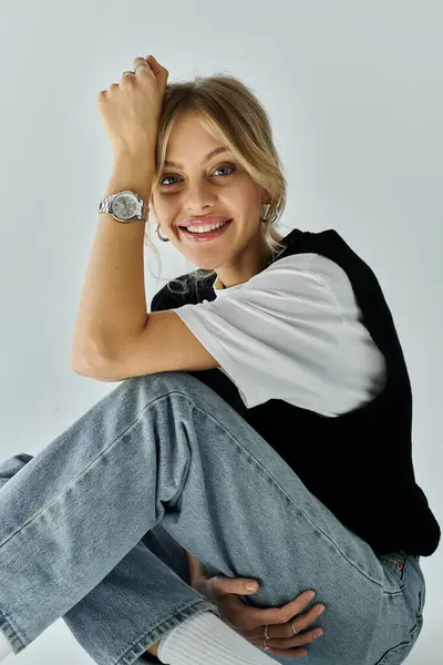 stock image A stylish young woman with blonde hair sits on the ground, elegantly showcasing a wristwatch on her wrist.