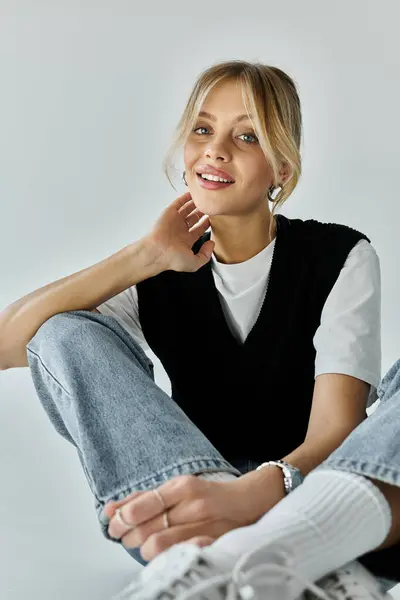 stock image A stylish, young woman sits gracefully with her legs crossed on a grey background.