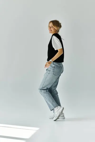 stock image A stunning young woman with blonde hair stands gracefully in a white room, hands nonchalantly tucked in her pockets.