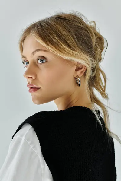 stock image A stylish young woman with blonde hair wearing a black and white sweater and earrings against a grey backdrop.