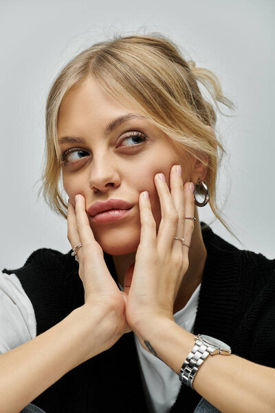 Молодая женщина с светлыми волосами в стильной повседневной одежде, глубоко созерцая, держа лицо руками.