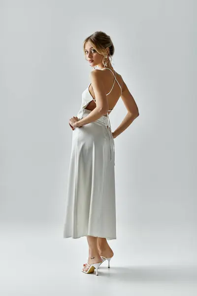 stock image A young woman with blonde hair poses in a white dress against a grey backdrop.