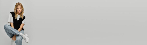 Стильная молодая женщина с светлыми волосами элегантно позирует на стуле на сером фоне.