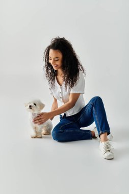 Genç bir kadın küçük beyaz Bichon Frise köpeğini nazikçe okşar..