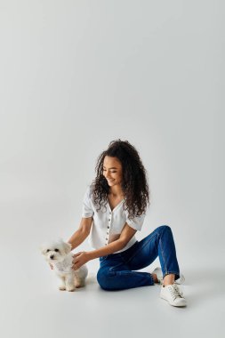 Woman seated on floor, tenderly petting small white dog. clipart