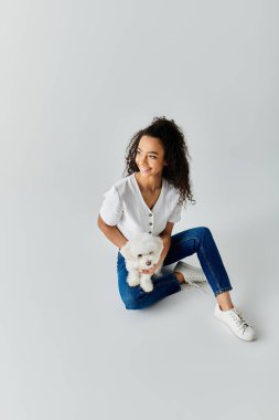 Bir kadın yerde oturuyor, nazikçe sevgili Bichon Frise köpeğini tutuyor..