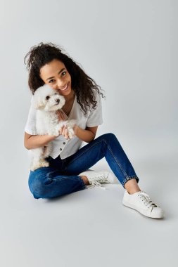 Woman seated on floor, holding white dog. clipart