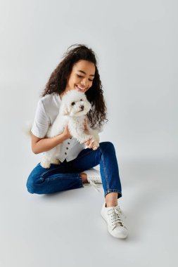 A woman peacefully sits on the floor, tenderly holding her white dog. clipart