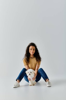 Bir kadın yerde huzur içinde oturuyor, pofuduk köpeğiyle bağ kuruyor..