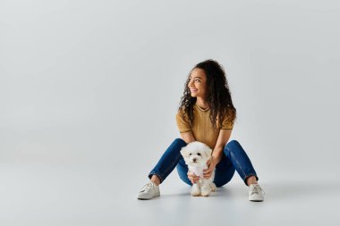 Bir kadın yerde, beyaz köpeğinin yanında huzur içinde oturuyor..
