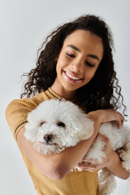 Genç bir kadın nazikçe beyaz bir köpeği kollarında tutuyor..