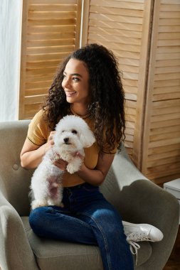 Kadın, sandalyeye oturmuş, beyaz köpeği tutuyor..