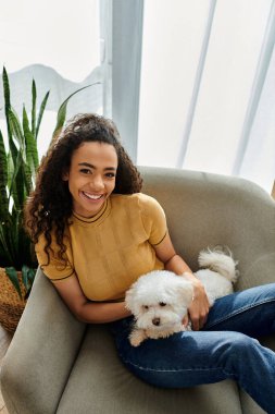 Sandalyede oturan beyaz köpek tutan kadın.