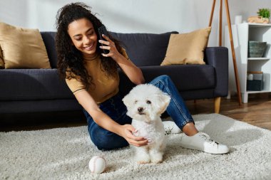 Yerde oturan kadın, beyaz Bichon Frise köpeğini sevgiyle okşuyor..