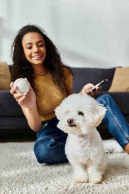 Woman peacefully sits with her white bichon frise on the floor. clipart