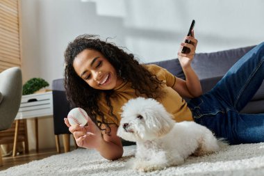 Bir kadın bichon friz 'iyle uzanıp telefonunu kontrol ediyor..
