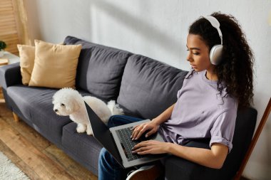 Woman relaxing on couch with laptop, accompanied by bichon frise dog. clipart