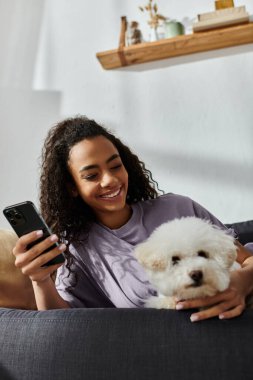 Oturmuş koltukta pofuduk beyaz köpeğe sarılmış bir kadın..