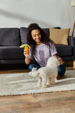 Genç bir kadın, kabarık tüylü köpeğiyle yerde keyifle etkileşime girer..