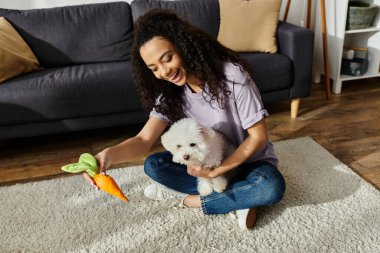 Bir kadın oturuyor, kabarık tüylü Bichon Frise köpeğiyle yerde kaynaşıyor..