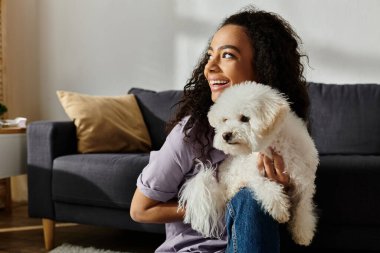 Kollarında tüylü beyaz bir köpekle kanepede dinlenen bir kadın..