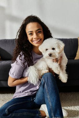 Yerde oturan bir kadın, sakin bir anda beyaz köpeğini tutuyor..