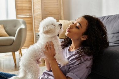 Genç bir kadın kanepede dinleniyor, beyaz köpeğini nazikçe tutuyor..