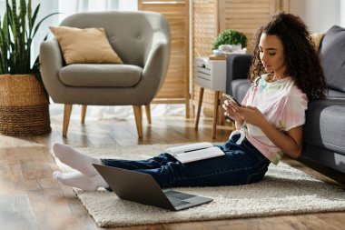 Yerde oturmuş dizüstü bilgisayarla etkileşime geçen bir kadın..