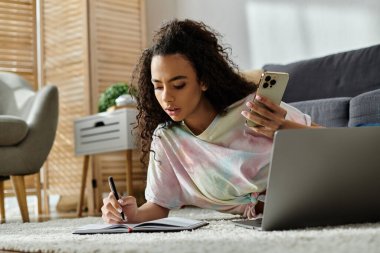 Yerde yatan kadın dizüstü bilgisayar ve cep telefonuyla birden fazla iş yapıyor..