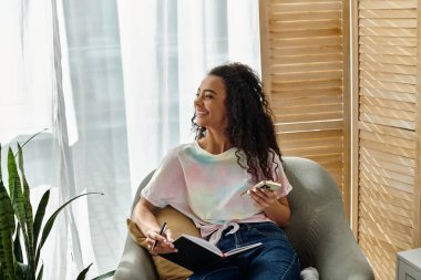 Sandalyede kitap okuyan ve kalemle yazan genç bir kadın..