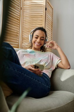 A woman relaxes on a couch while listening to music. clipart