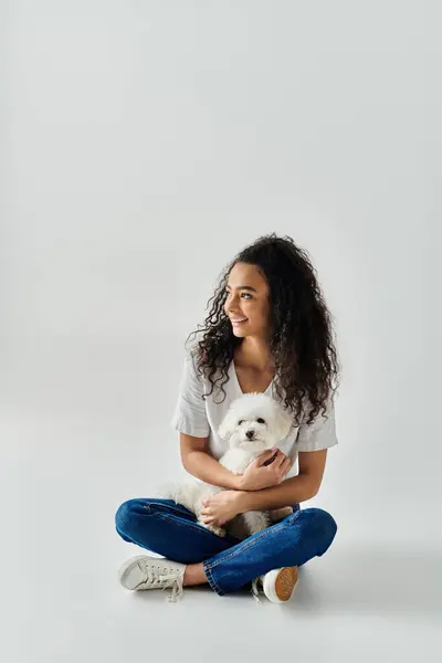 stock image A woman sitting on the floor, peacefully holding her white dog.