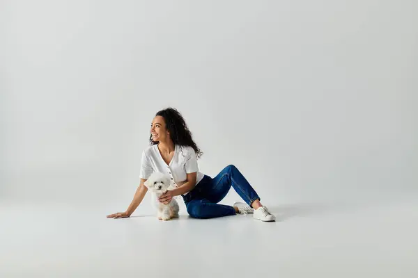 stock image Woman sitting on ground, gently holding her bichon frise dog.