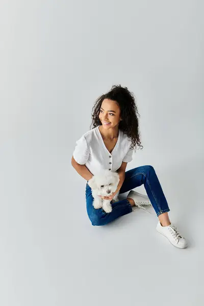 stock image A woman sits on the ground, tenderly holding her beloved Bichon Frise dog.