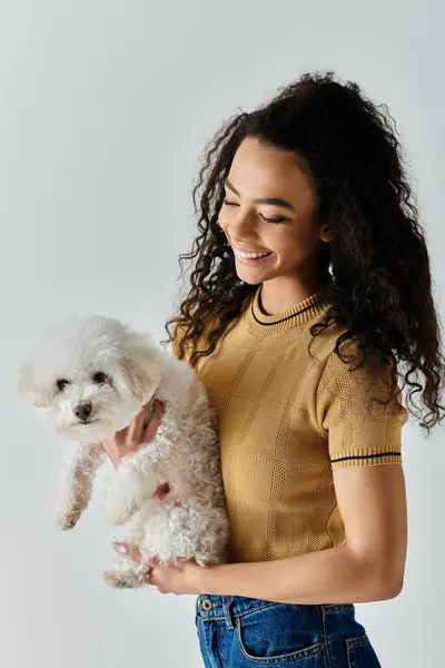 stock image A young woman tenderly holds a fluffy white Bichon Frise in her arms.