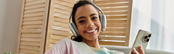 Женщина в наушниках наслаждается музыкой, сидя на диване.