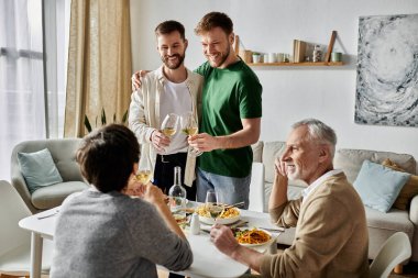 Eşcinsel bir çift, aile ile birlikte bir evde yemek masasında kadeh kaldırıyor..