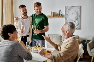 A gay couple toasts with parents during a dinner at home. clipart