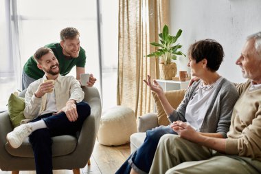 A gay couple sits with parents on a couch, enjoying a conversation and a cup of coffee. clipart