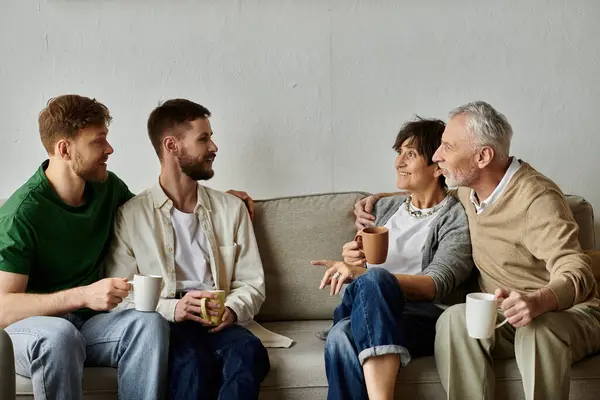 stock image A gay couple sits on a couch with parents, all enjoying coffee together.