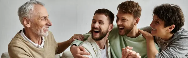 stock image A gay couple sits with parents at home, all laughing together.