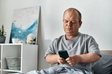 Kapsamlı bir adam modern bir dairede yatağında telefonuna bakıyor..