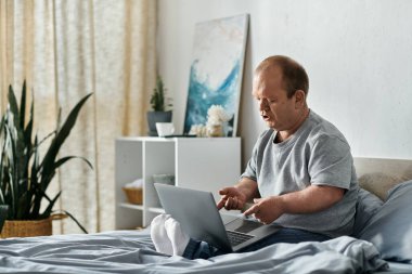 Kapsayıcı bir adam yatağında oturuyor, dizüstü bilgisayarına dalmış..