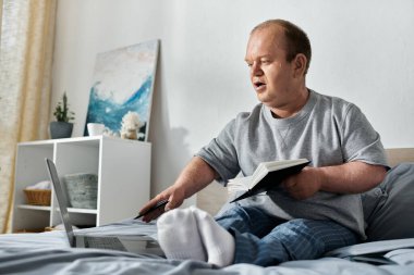 A man with inclusivity sits in bed, working on a laptop and holding a book. clipart