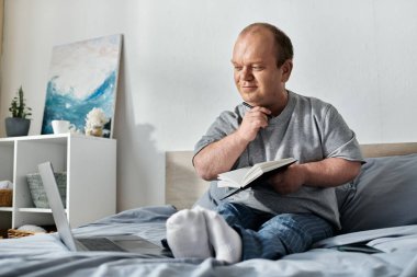 Kapsamlı bir adam yatakta oturur, düşünceli bir şekilde elinde bir defter ve kalemle, gününü yansıtır..