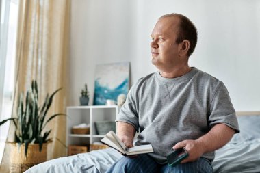 Kapsamlı bir adam bir yatakta oturur, pencereden dışarı bakar, elinde bir defter ve bir telefon tutar..