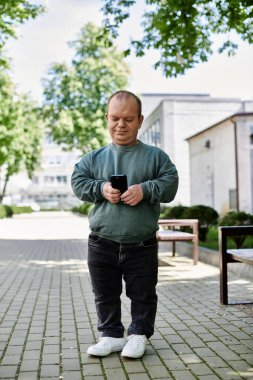 Kapsamlı bir adam şehir caddesinde yürüyor, telefonunu kontrol ediyor ve güneşli bir günün tadını çıkarıyor..
