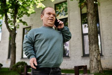 Yeşil kazaklı bir adam binanın dışında telefonuyla konuşuyor..